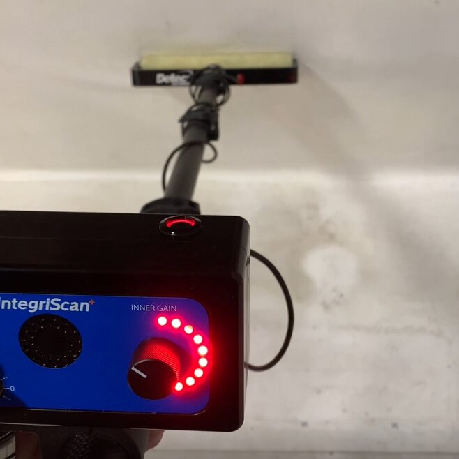 Electronic Leak Detection Vertical Scanning Unit being used to scan a vertical surface and successfully locating a breach, communicated by the lights on the unit.